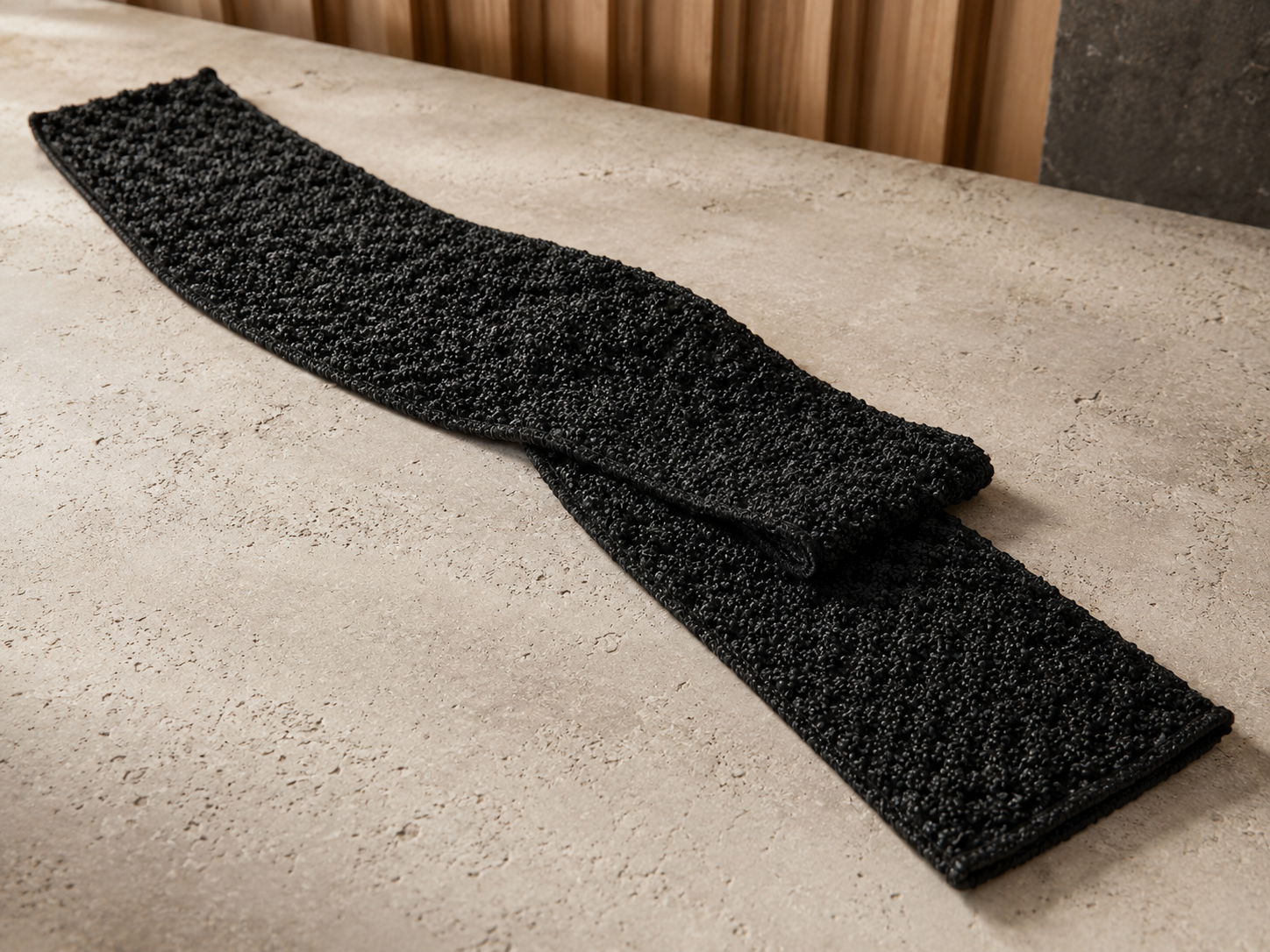 Complete black Kuyona towel arranged on warm stone to show its full length, width and flexible construction