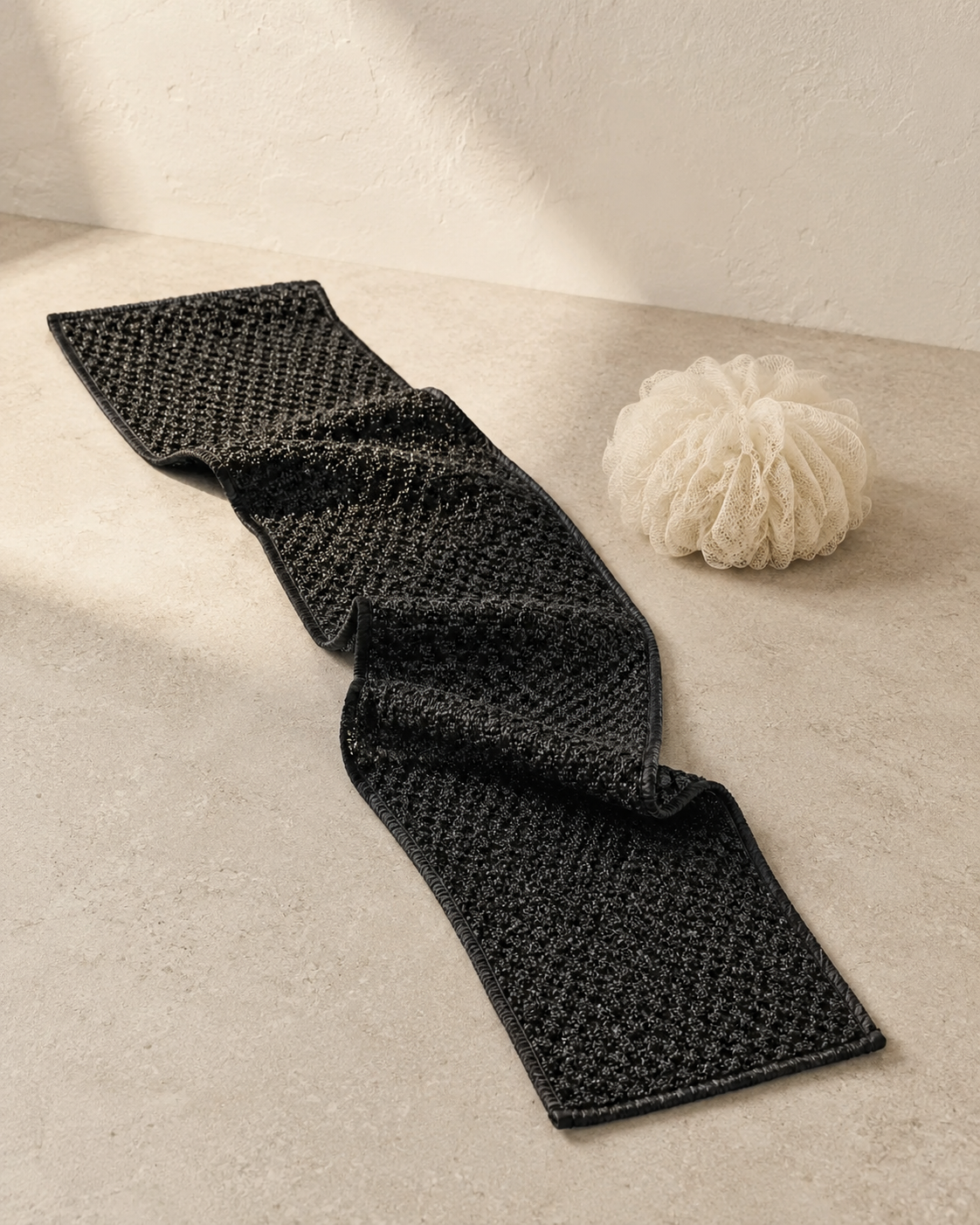 Complete black Kuyona towel arranged on warm stone to show its full length and flexible shape